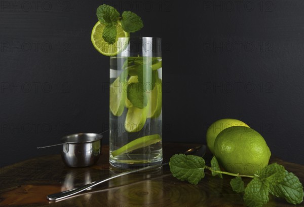 Glass of Mojito cocktail with mint and lime on a black board with fresh limes. Sparkling refreshing water. Place for text