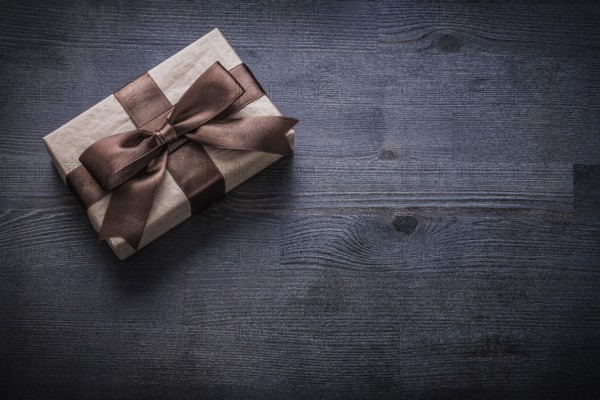Present box-container with brown tied bow on vintage wooden board