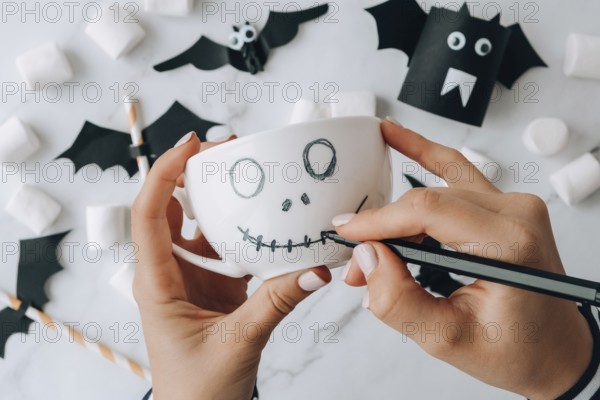 Female hands paint on white cup scary jacks face DIY for kids Halloween home activities Holiday art children craft Handmade decorations. Step by step Socially distanced at home Idea for art class