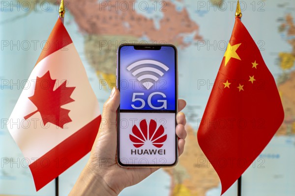 Calgary, Alberta, Canada. Sep 8, 2020. A person holding an iPhone with a 5G and Huawei logo on the screen next to a Canada and China flags on a world map