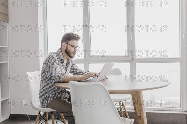 Man in a checkered shirt working on a laptop in a bright, modern room