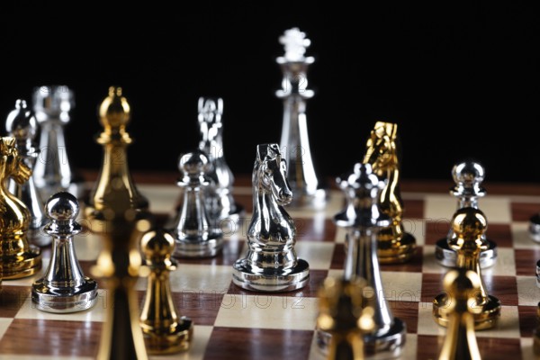 Gold and silver chess figures standing on chessboard. Intellectual and tactic game. Strategy planning, leadership and teamwork business concept. Close-up metal chess pieces on black background
