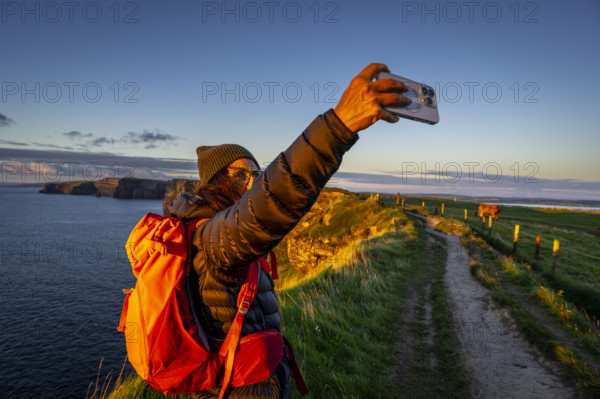 Female hiker taking a selfie, Cliffs of Moher, The Burren, County Clare, Ireland, United Kingdom, Europe