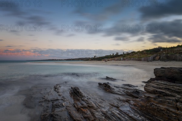 Sunset over the picturesque white sand beach and turquoise waters at La Pelosa Beach with rocks in the foreground