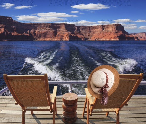 Waves from the boat cut through the Lake Powell. At the stern of the vessel are two deck chairs. On the back of one hanging elegant ladies straw hat