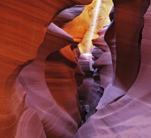 A thin ray of sunlight illuminates the sandy bottom of the canyon. Noon in a red-orange Antelope Canyon