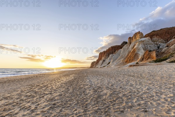 Incredible rock formations by the sea. Red cliffs with red earth and breathtaking formations on the wide sandy beach, which is bathed in warm light by the sun at sunset. Praia da Falésia, Algarve, Portugal, Europe