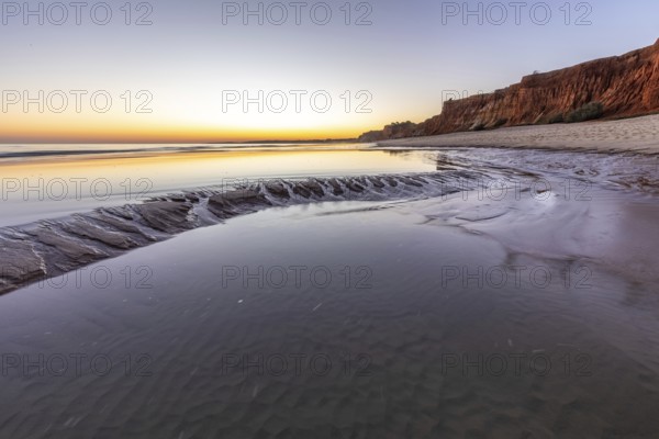 Sea with reflection at low tide in the calm waters of the Atlantic. Landscape shot of the sunset on the cliffs and the sandy beach of Praia do Poço Velho, Praia da Falésia, Quarteira, Algarve, Portugal, Europe