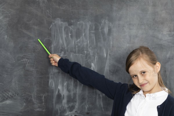 Schoolgirl shows on an empty school board. He is standing in the classroom at the chalkboard. Younger girl