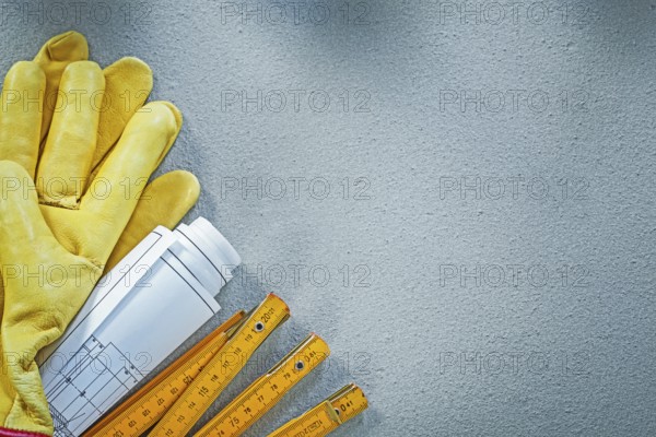 Composition of working gloves blueprints wooden meter on concrete background building concept