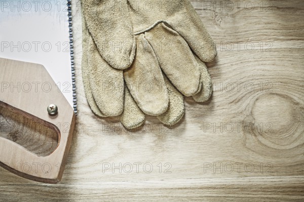 Safety gloves handsaw on wooden board top view construction concept