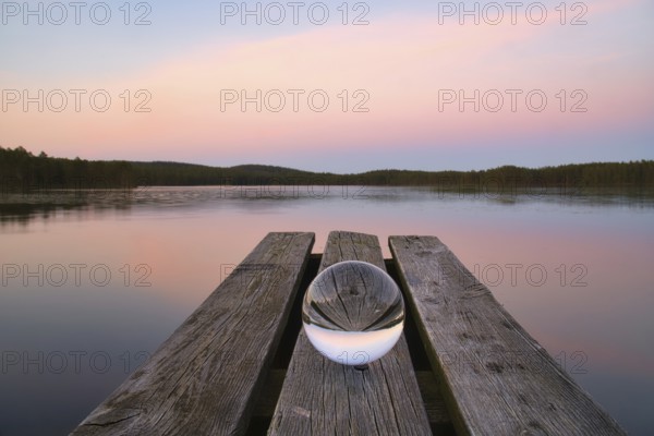 Glass ball on a wooden pier at a Swedish lake at evening hour. Nature shot from Scandinavia