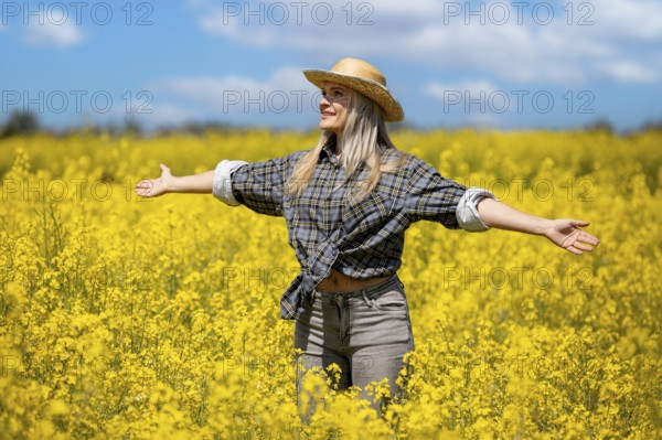 A cheerful woman is joyfully surrounded by a vast field filled with bright yellow flowers under a clear blue sky