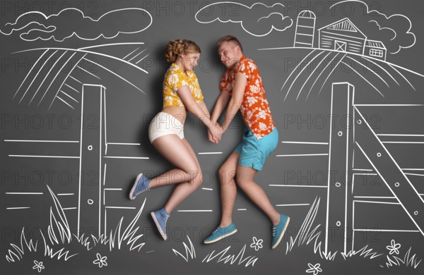 Happy valentines love story concept of a shy romantic couple sitting on a hedge and holding hands against chalk drawings background of a landscape in summer