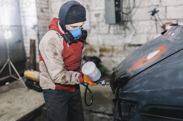 Worker spray painting a car hood in a workshop environment
