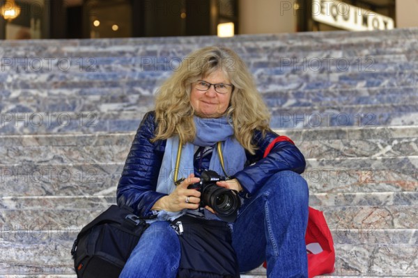 Woman sitting casually with camera on stairs and seems to concentrate on photography, Manhattan, New York, USA, North America