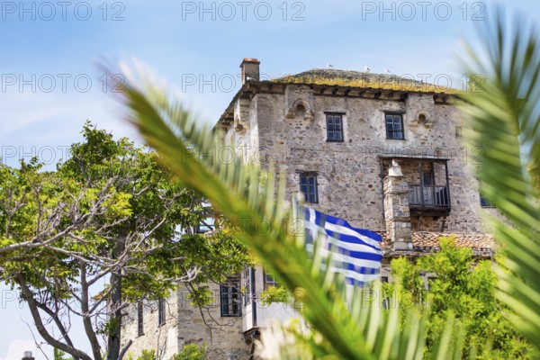 Ancient Ouranoupolis Tower on Athos peninsula in Halkidiki, flag of Greece. View through the palm leaves