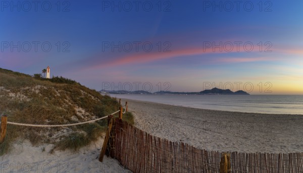 Picturesque Playa del Muro beach with sand dunes and a view of the historic maritime observation towers and the town of Alcudia in the background