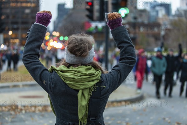 Young woman is raising her arms high while looking at the crowd during an ecological protest. Shot from the back