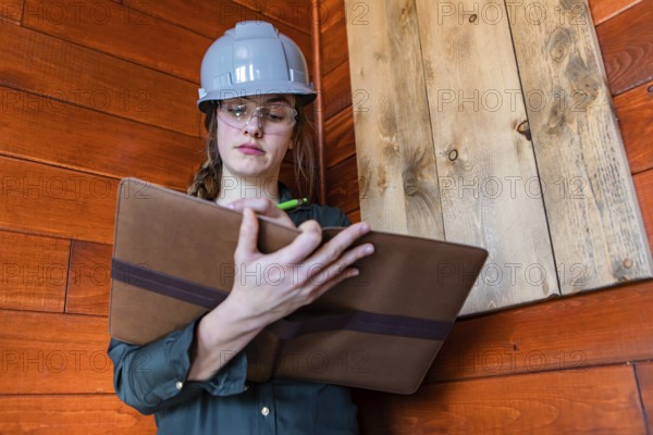 Construction female inspector using a clipboard to taking notes. a young caucasian woman worker wearing hard hat at work, low angle portrait