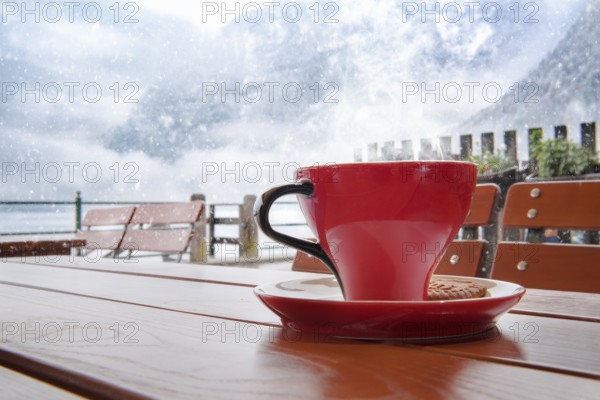 Relaxing moment with a hot cup of coffee, on a table, at an Austrian restaurant, in Hallstatt, with a view over the Dachstein Mountains, while outside is snowing heavily