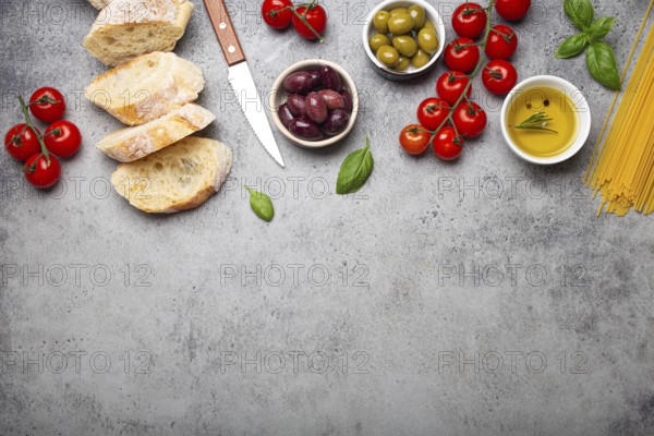 Food composition with sliced ciabatta, olives, olive oil, spaghetti, fresh basil, cherry tomatoes on gray concrete stone rustic background top view, copy space. Italian cuisine concept, food photography, food photography