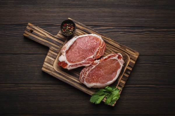 Cut raw meat pork steaks with seasonings on kitchen cutting board, rustic wooden background top view, ready for BBQ. Pork loin chops, food photography, food photography