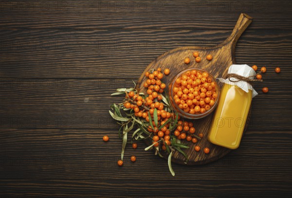 Sea buckthorn healthy drink in bottle, ripe berries in glass jar and branches with leaves top view on dark wooden rustic background, great for skin, heart, vessels and immune system. Copy space, food photography, food photography