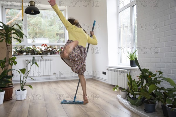 A girl dances with a mop to clean the floor in a new house, general cleaning in an empty room, the joy of moving, help with the housework
