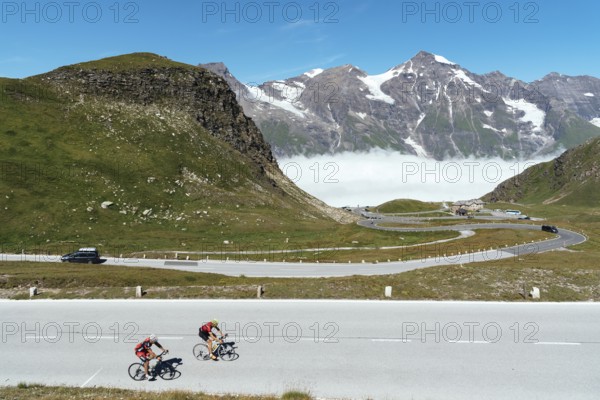 Grossglockner, Austria, August 7, 2017: Cyclists climbing mountain pass by Alpine road through valley with sea of clouds. Grossglockner, Austria, Europe