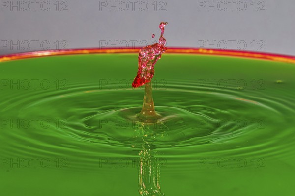 A red water drop rises dynamically on a green background, water drop, collision, high-speed photography, concept, water figures