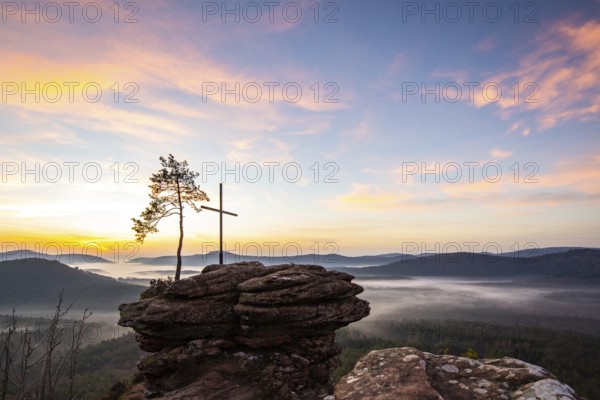 Landscape shot of nature in the morning. Mist in the valley and a summit cross on a sandstone cliff. Sunrise in the Palatinate Forest, Germany, Europe