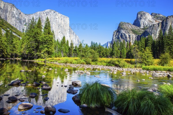 Picturesque El Capitan and mountain peaks are reflected in the smooth water of the Merced River. Beautiful day in the park valley. Yosemite Park is located on the slopes of the Sierra Nevada