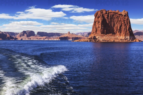 Foamy trace of a motor boat crosses the emerald waters. In the distance the coast of red sandstone. Lake Powell on the Colorado River
