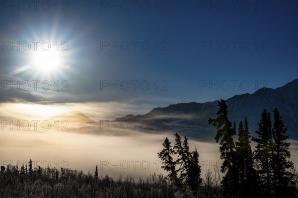 Sun over foggy, snow-covered landscape with mountain silhouette, Yukon, Canada, Kluane National Park, North America