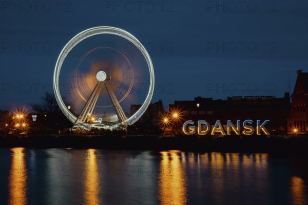 Gdansk Poland Ferris wheel in the old town of Gdansk at night evening dusk Reflection in river water Europe. Long exposure photo. City scenic view Illuminated attraction park and street with beautiful reflection on the water. Travel destination tourist attraction