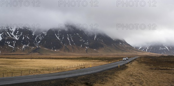 Straight highway country road with cars moving and mountains covered in mist in Iceland. Road is part of Icelandic Ring Road