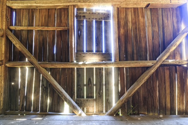 The interior of an old barn with sunlight streaming in through the boards