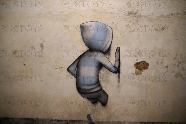 A lonely boy with a hood stands in front of a plain wall, creating a calm and minimalist atmosphere, MAUSA VAUBAN, Museum of Urban Art and Street Art, Neuf-Brisach Fortress, France, Europe