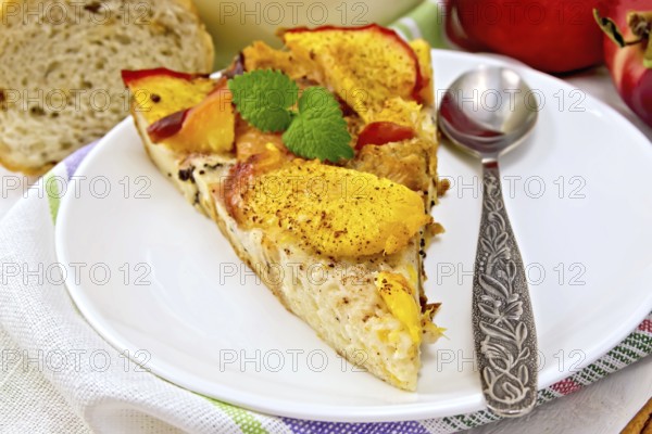Sweet bread pudding of peaches with milk and eggs, a spoon in a plate on a linen towel, milk in glass jug, cinnamon on a wooden boards background