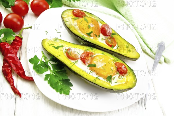 Scrambled eggs with cherry tomatoes in two halves of avocado in a plate, towel and fork on white wooden board background