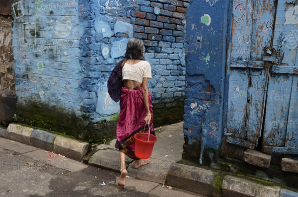 Woman with bucket walking in narrow lane, Kolkata, West Bengal, India, Asia