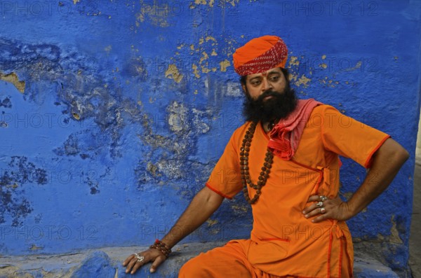 Priest saffron sitting against blue wall, Jodhpur, Rajasthan, India, Asia