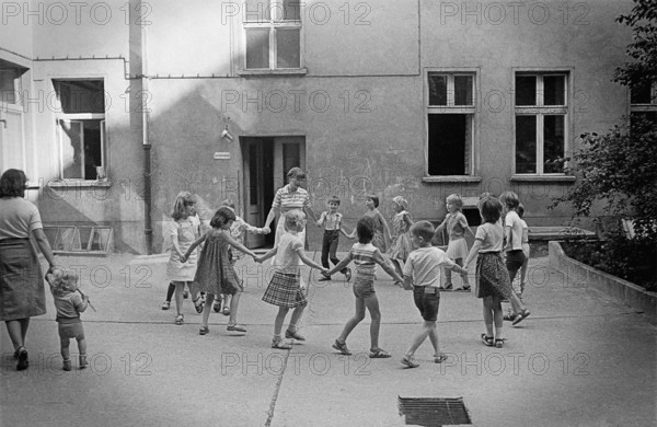 26/04/1983 GDR East Berlin district of Prenzlauer Berg. Children dancing in a circle with their teacher in a backyard in Lettestrasse. Berlin