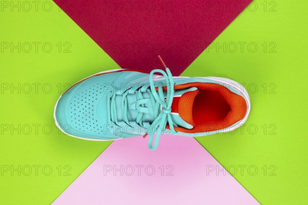 Red, cyan, white new tennis shoe in studio shot over green, pink, purple background. Directly from above