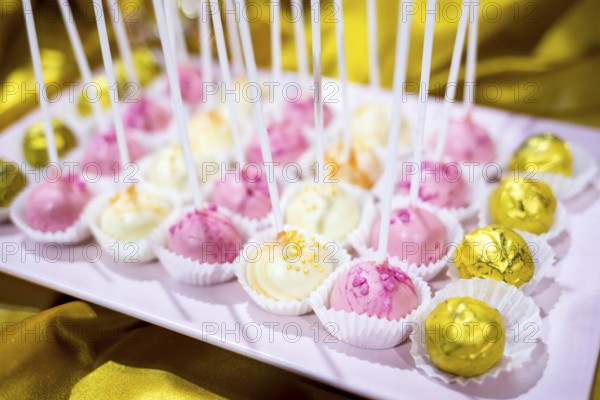 Different colourful candies on a stick. Bonbons wrapped in golden foil. Yellow, pink, white. Extremely tasty and delicious desserts. Sweets full with sugar. Unhealthy food diet