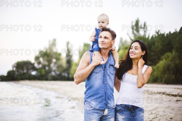 Beautiful young family on holiday with baby. The father holds the blonde girl in her arms, and the brunette's mother hugs her husband. The concept of a family beach holiday summer near the sea