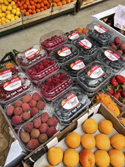 Budva, Montenegro - 25 december 2022: Fresh lychee berries, peaches, currents, raspberry blueberries in boxes lie on the counter