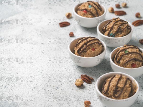 Safe-to-eat raw monster cookie dough in small portion bowl and nuts on gray cement background. Ideas and recipes for kids and toddlers meal. Copy space for text