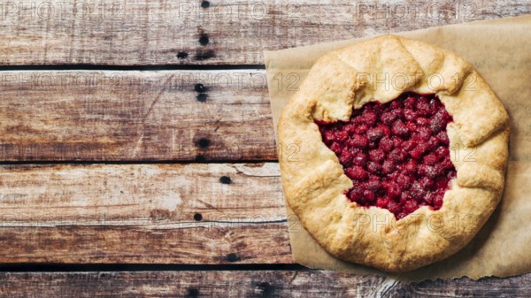 Perfect raspberry galette. Delicious rustic homemade tart with frozen or fresh raspberries on old wooden background. Beautiful round shape galette with raspberries, copy space. Top view or flat lay